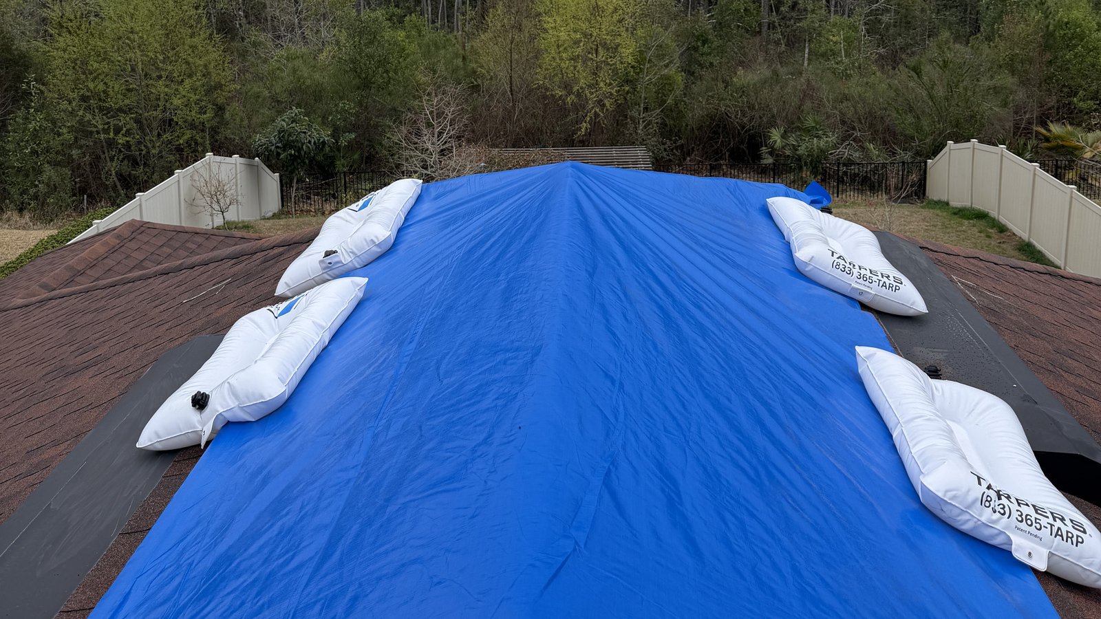Blue emergency roof tarp anchored with white TarpBags® along both edges of a shingle roof