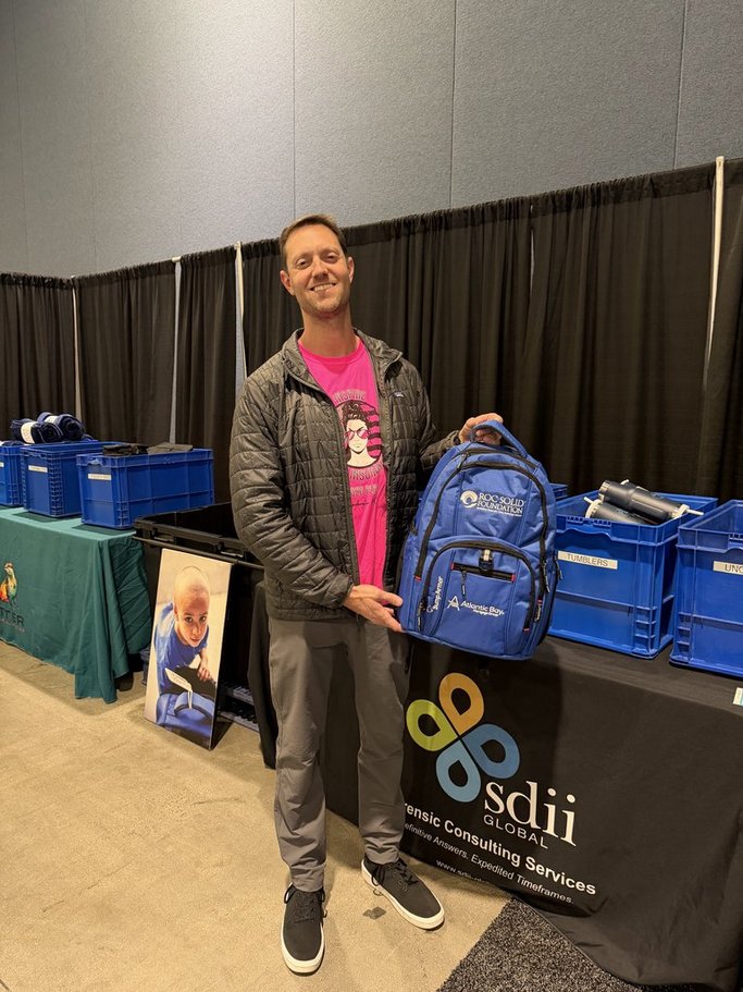 Tarpers team member holding a Roc Solid Foundation backpack assembled at the PLRB 2026 conference charity event